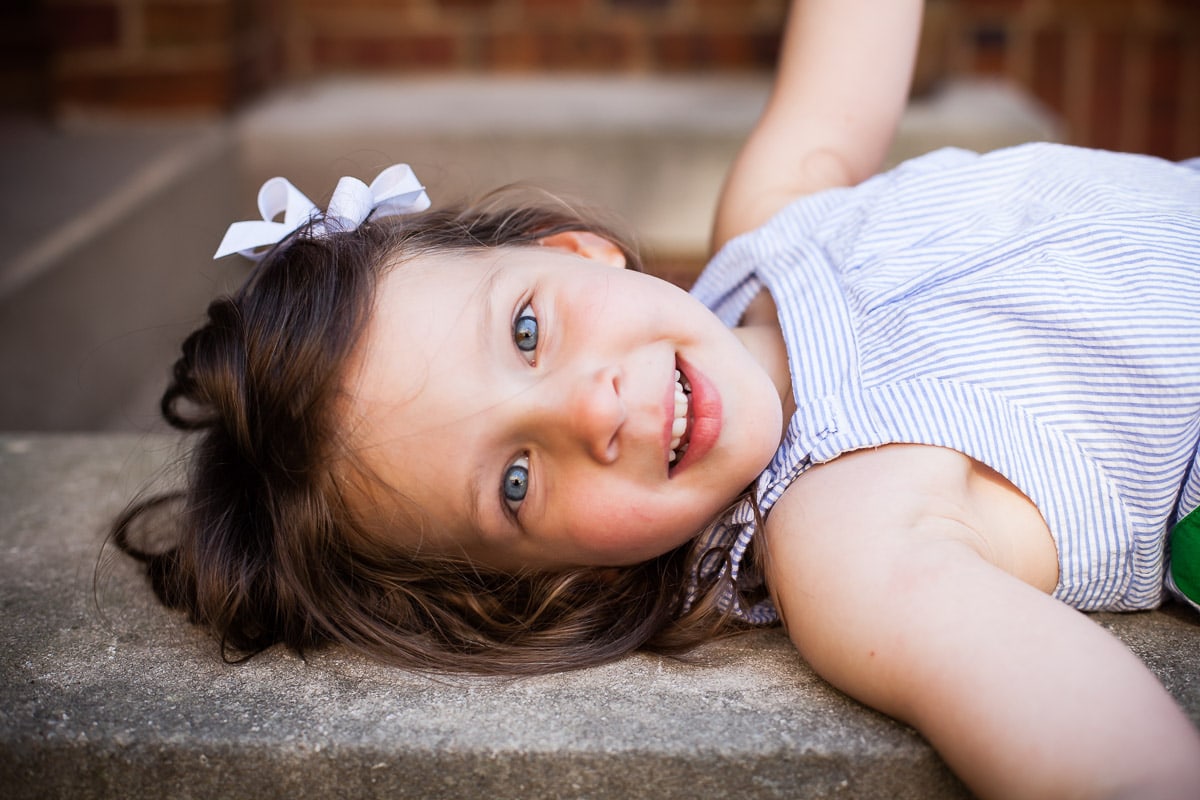Little girl lies on step outside house during a photo session on location at their home.