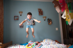 Freeze-motion photo of little boy jumping on the bed.