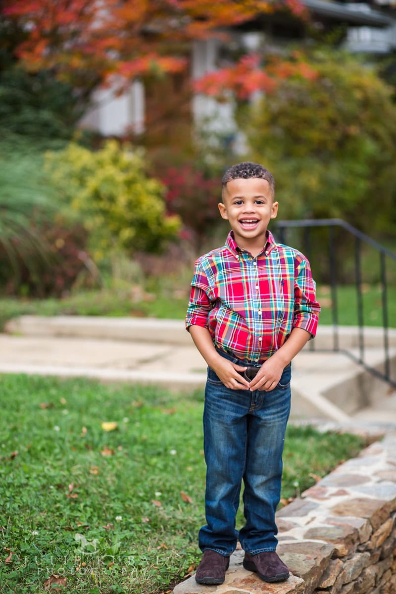 Little boy with plaid shirt dressed to coordinate with parents and sisters in family photos during outdoor fall session.