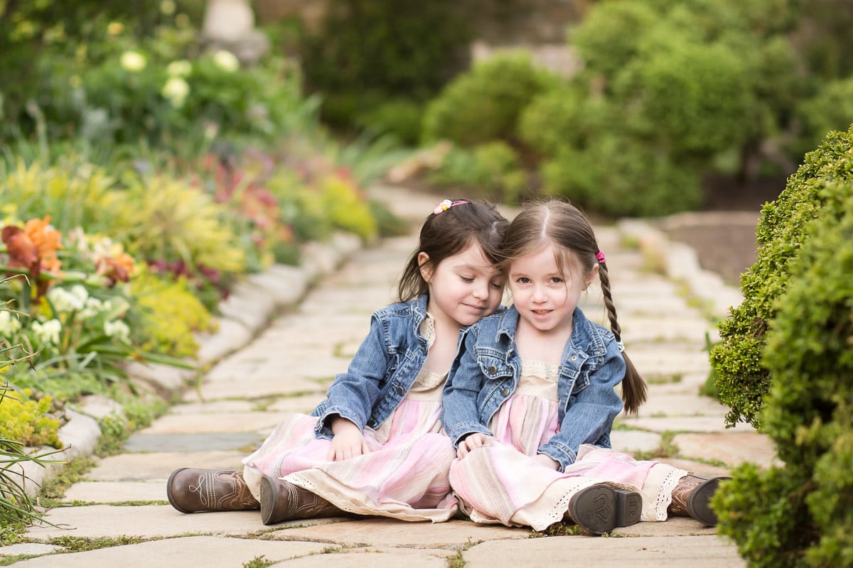Twin girls sit together on a stone walkway in Bishop's Garden at the Washington National Cathedral, one of my recommendations for spring photoshoot locations in DC