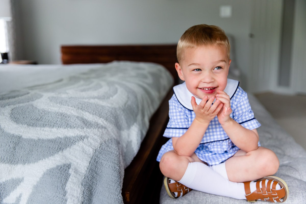 An example of one of my favorite child photo tips is not worrying about the subject making eye contact with the camera like in this photo of a  laughing little boy sitting on a bench at the foot of his parents' bed.