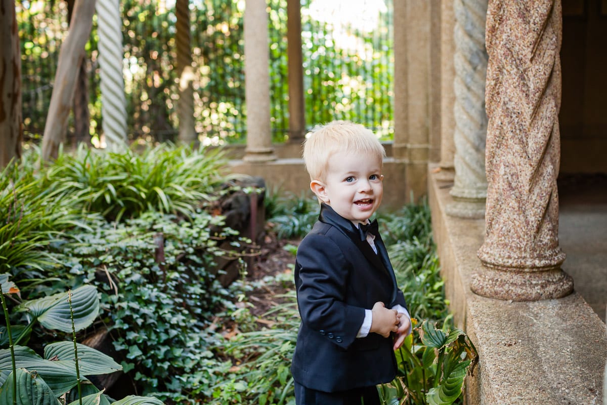Little boy dressed in a tuxedo stands in the garden at the Franciscan Monastery, one of the best spots in Washington DC for fall photos with the family.