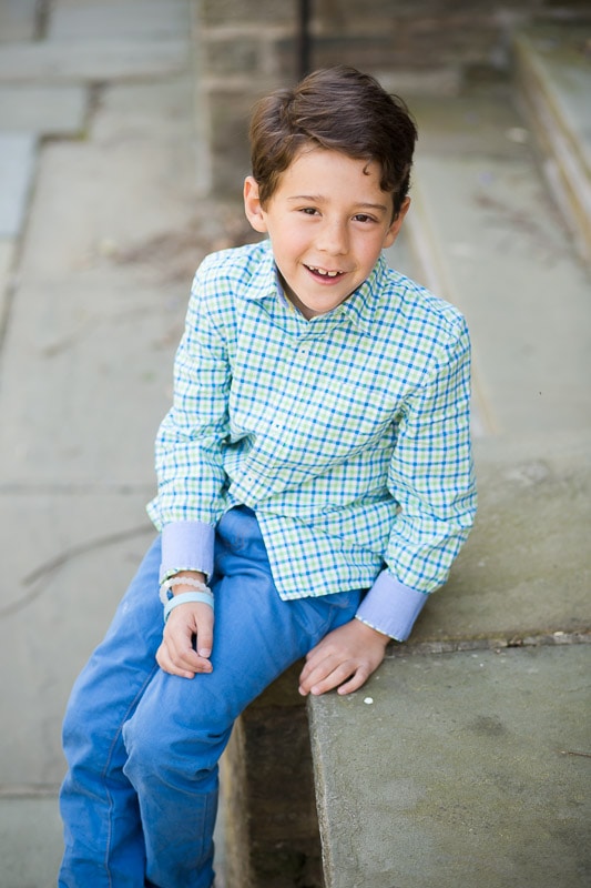Boy sitting on a stone wall in a garden behind Washington National Cathedral for photo session with his mom and siblings.