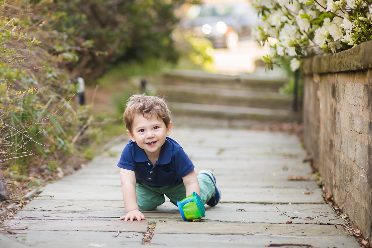 Toddler boy crawling on stone path pauses just long enough during this sibling photo session at the Washington National Cathedral