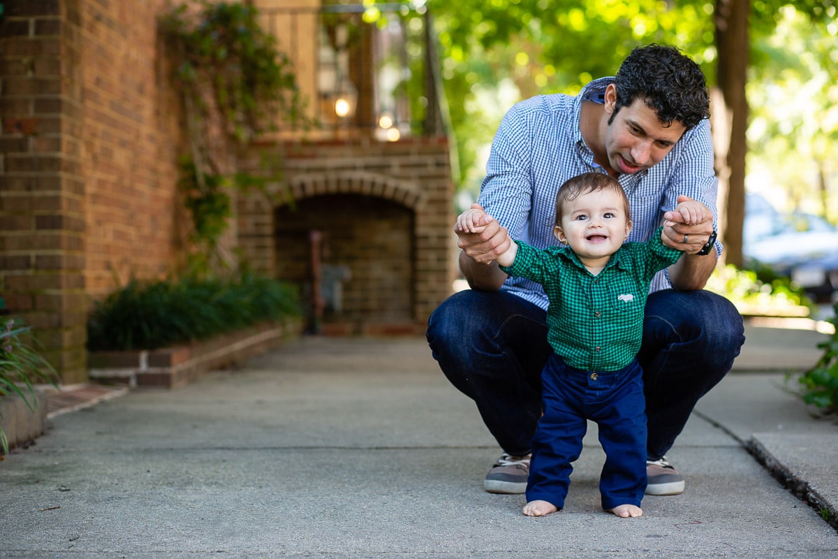 pick a family moment who can capture candid moments like this image of a father helping baby son stand on sidewalk. Image by best Alexandria, VA baby photographer Julie Kubal