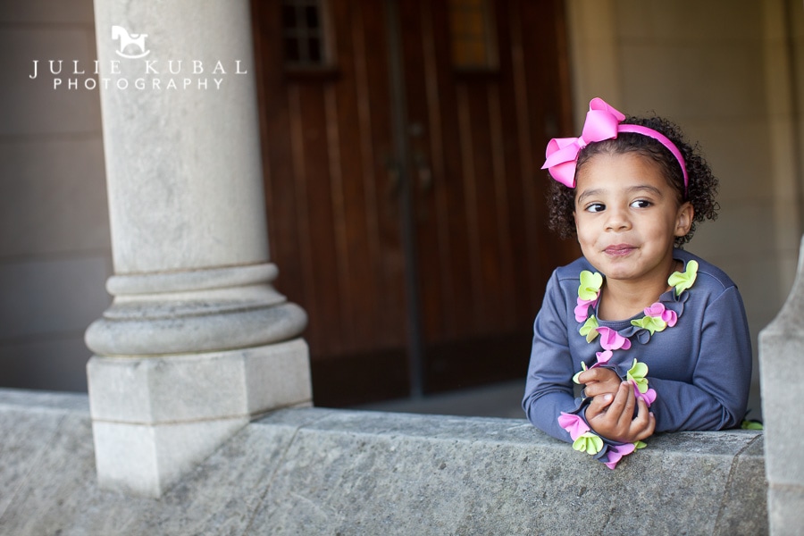 Little girl leans on a stone wall that is part of the exterior of Washington National Cathedral during a family photo shoot