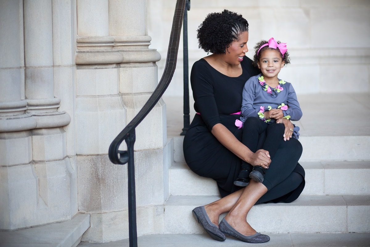 Pregnant mom sits with daughter on her lap on the steps outside Washington National Cathedral during their photo session with family photographer Julie Kubal