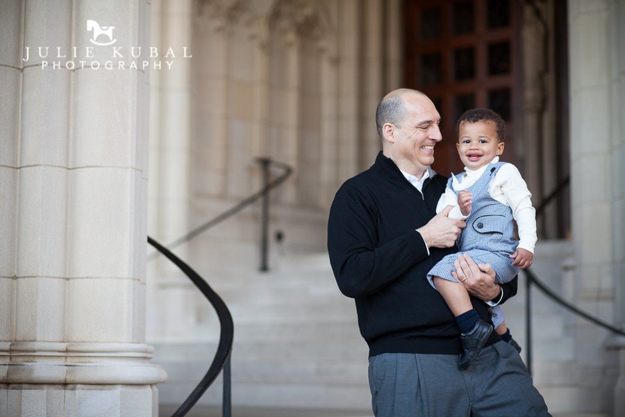 Father holding baby son stands on the stairs outside the National Cathedral during a family photo shoot.
