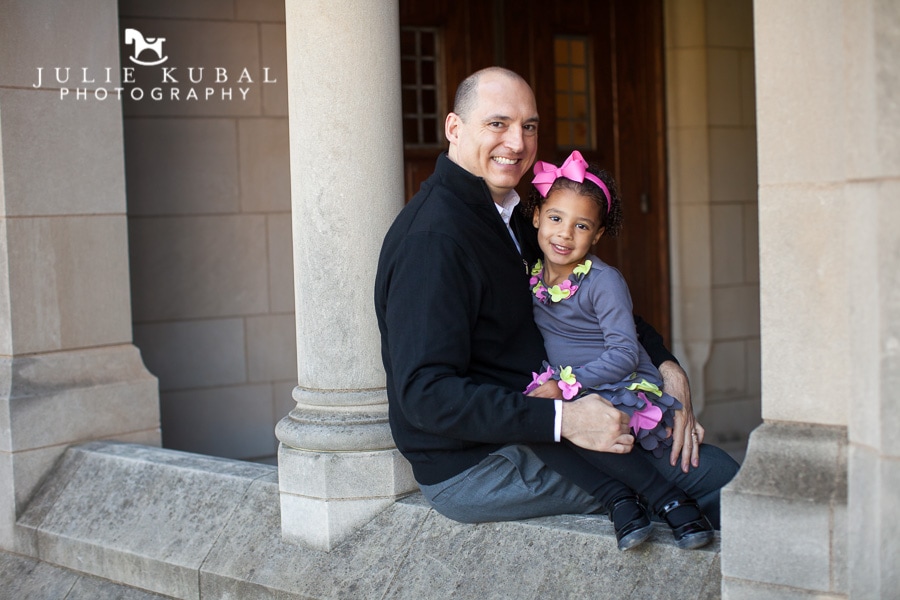 Father and daughter sit together on wall outside Washington National Cathedral during a photo session.