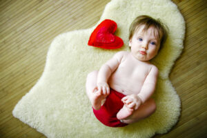 Baby girl lying on sheepskin rug with small heart-shaped pillow