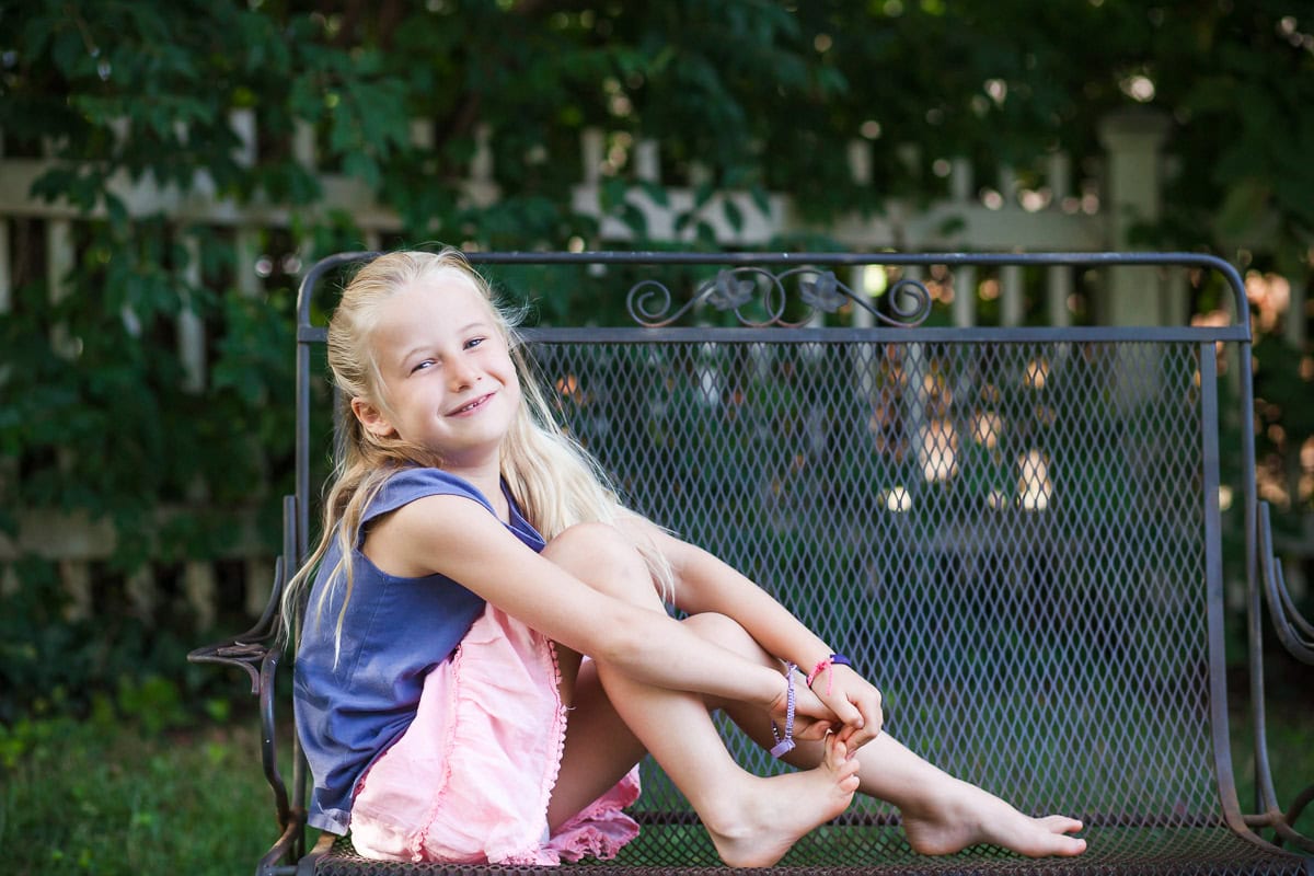 A little girl sitting on a bench during a family photo shoot .