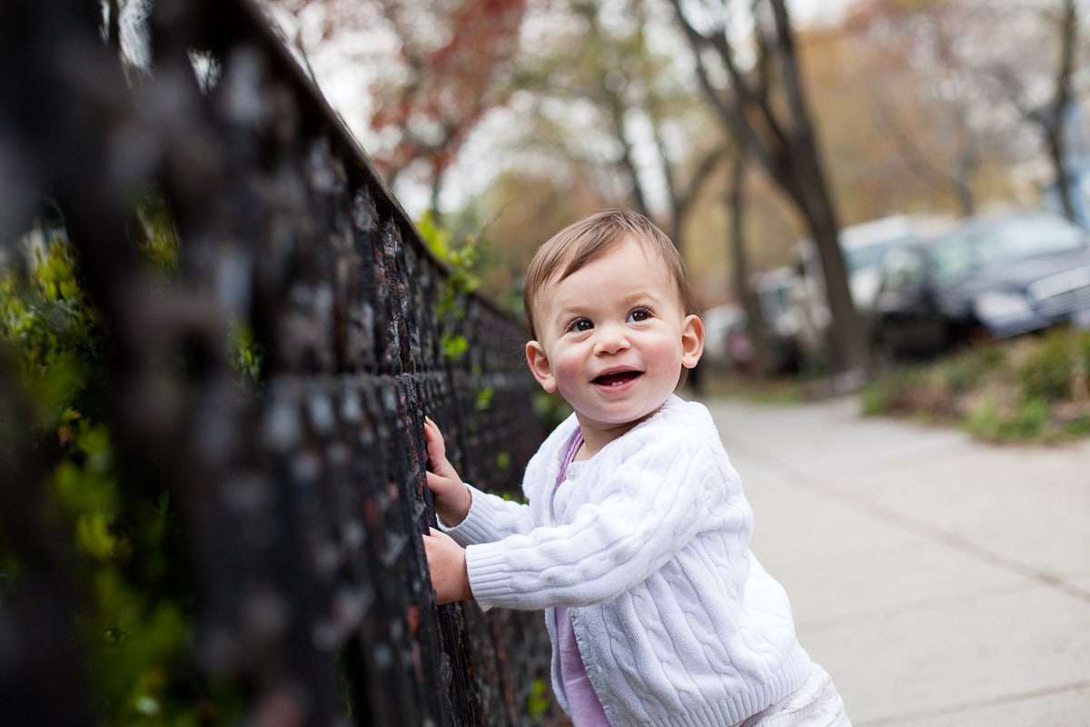 Toddler girl holds on to an iron fence in the Logan Circle neighborhood of Washington, DC. This is an example of one of my child photography tips to get on eye level with your subject rather than shooting from your full height.