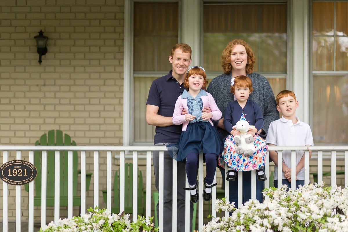A family of 5 poses for a photo on the porch of their home.