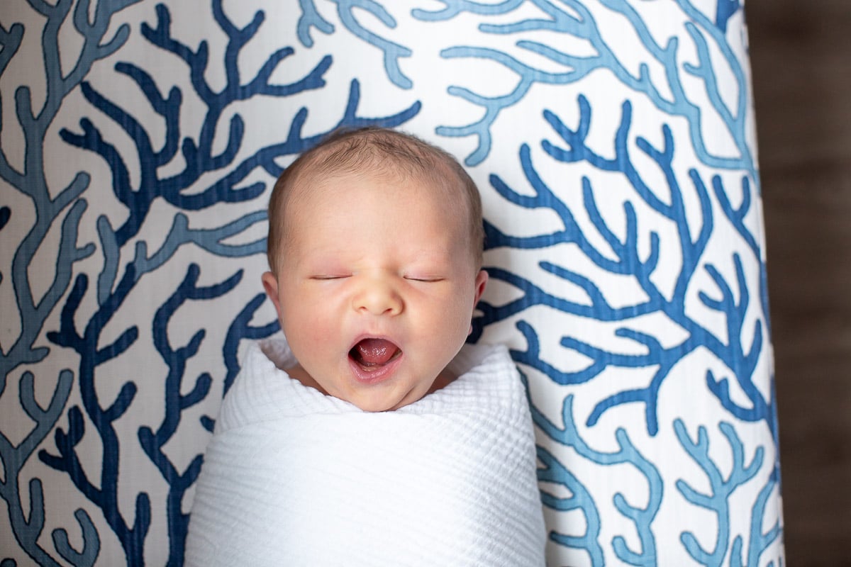 close-up photo of yawning newborn boy in white swaddle